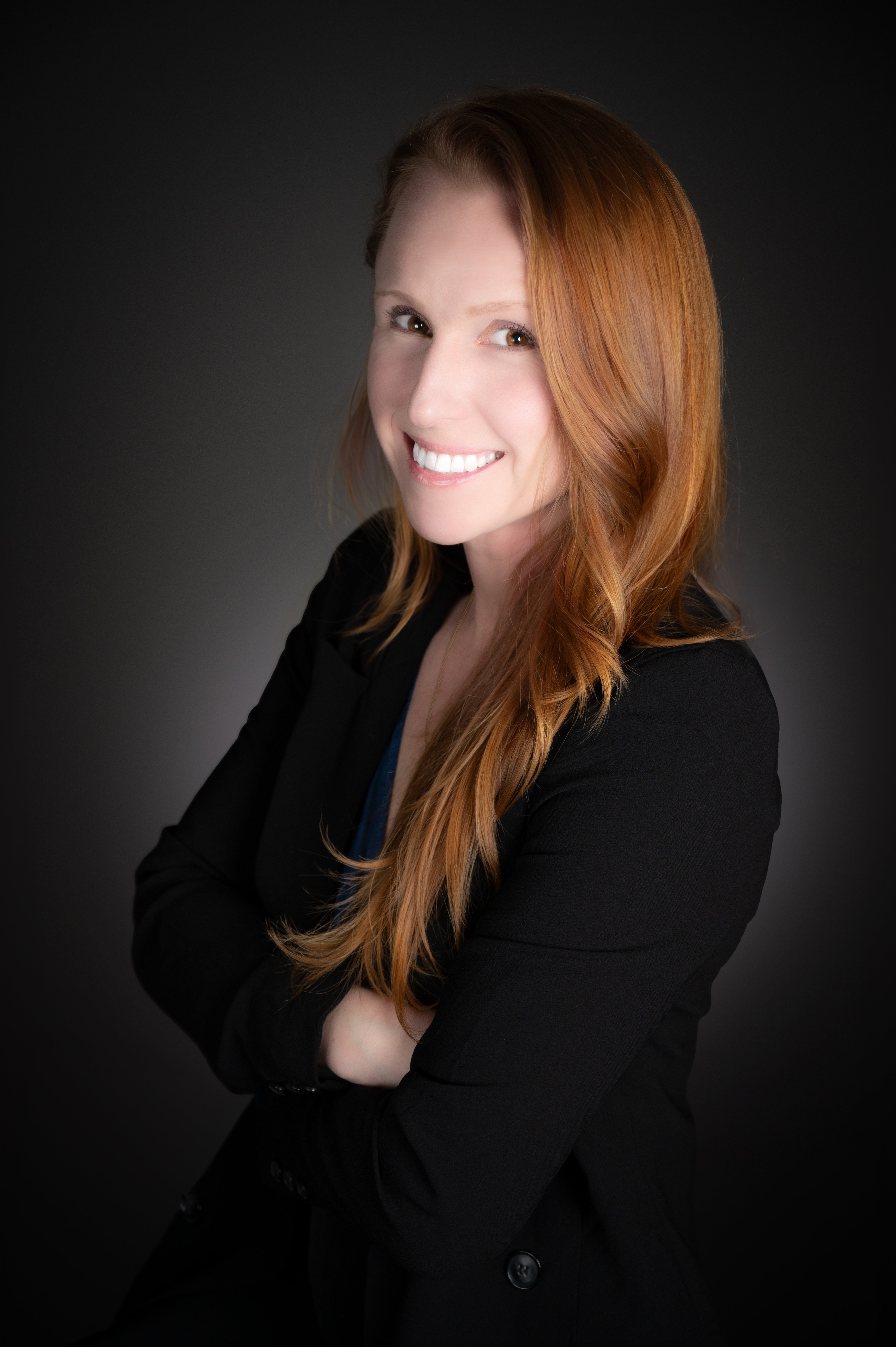 Woman, arms crossed, long orange hair, black top, dark background