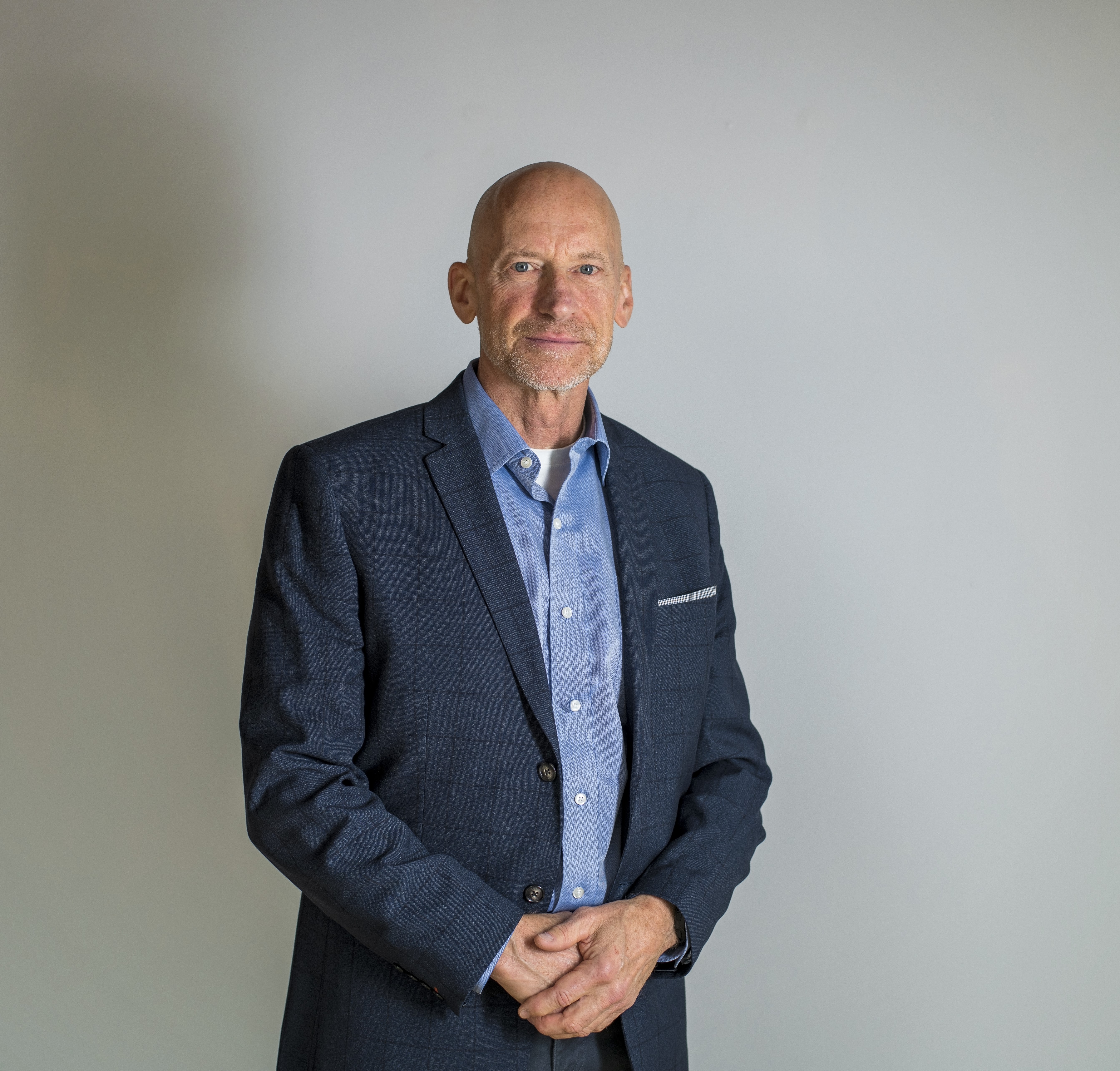 Man, blue sport coat and collar shirt, hands  standing with hands clasped in front, grey facial hair/beard