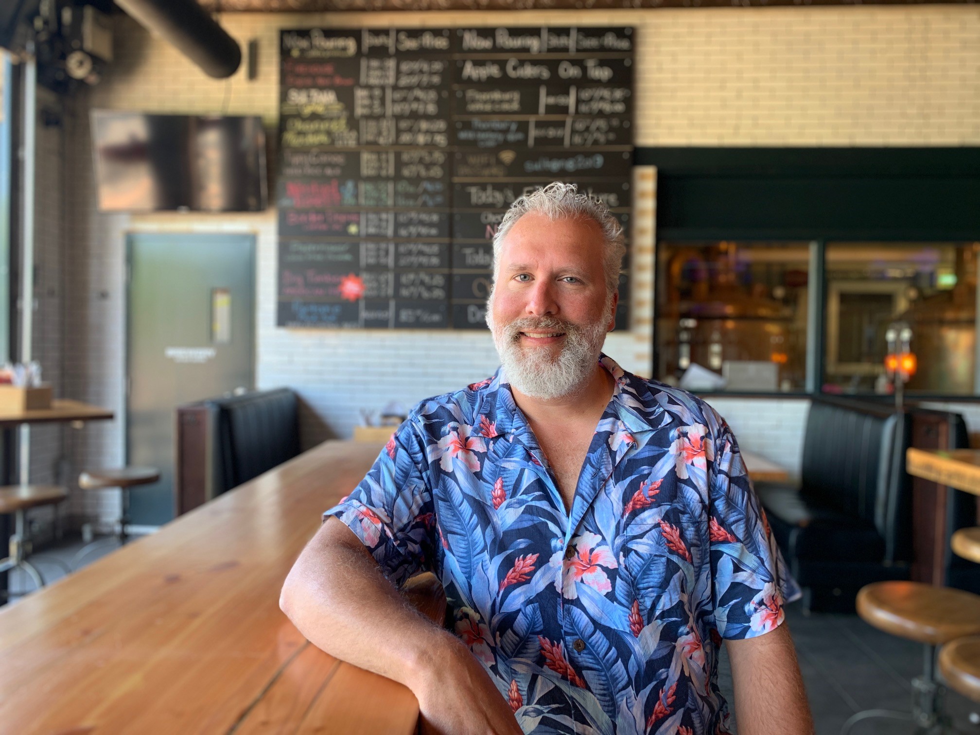 Man, flowered button up shirt, leaning on bar in restaurant