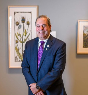 Man in blue suit purple standing in front a water colour painting on a brown wall