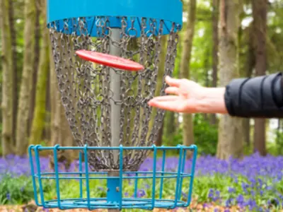 A persons hand throwing a disc into a disc golf net.