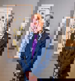 Man in blue suit purple standing in front a water colour painting on a brown wall