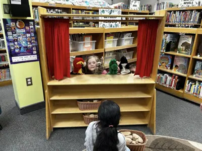 Two children put on a puppet show while a third watches.