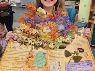 A child holds up a pop-up book displaying a large bouquet of flowers.