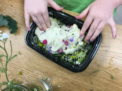 Child's hands mixing flower and plant pieces into homemade playdough during a Mini Farmer's session.