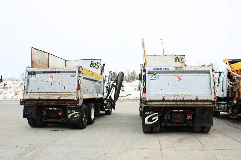 View of the back of 2 plow trucks with the names Plowasaurus-Rex and Goon Be Gone decalled on the back