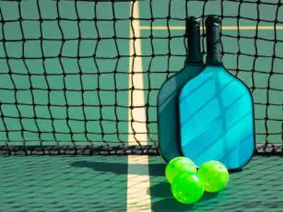 Blue pickleball paddle with 3 green balls in front of a net on a court.