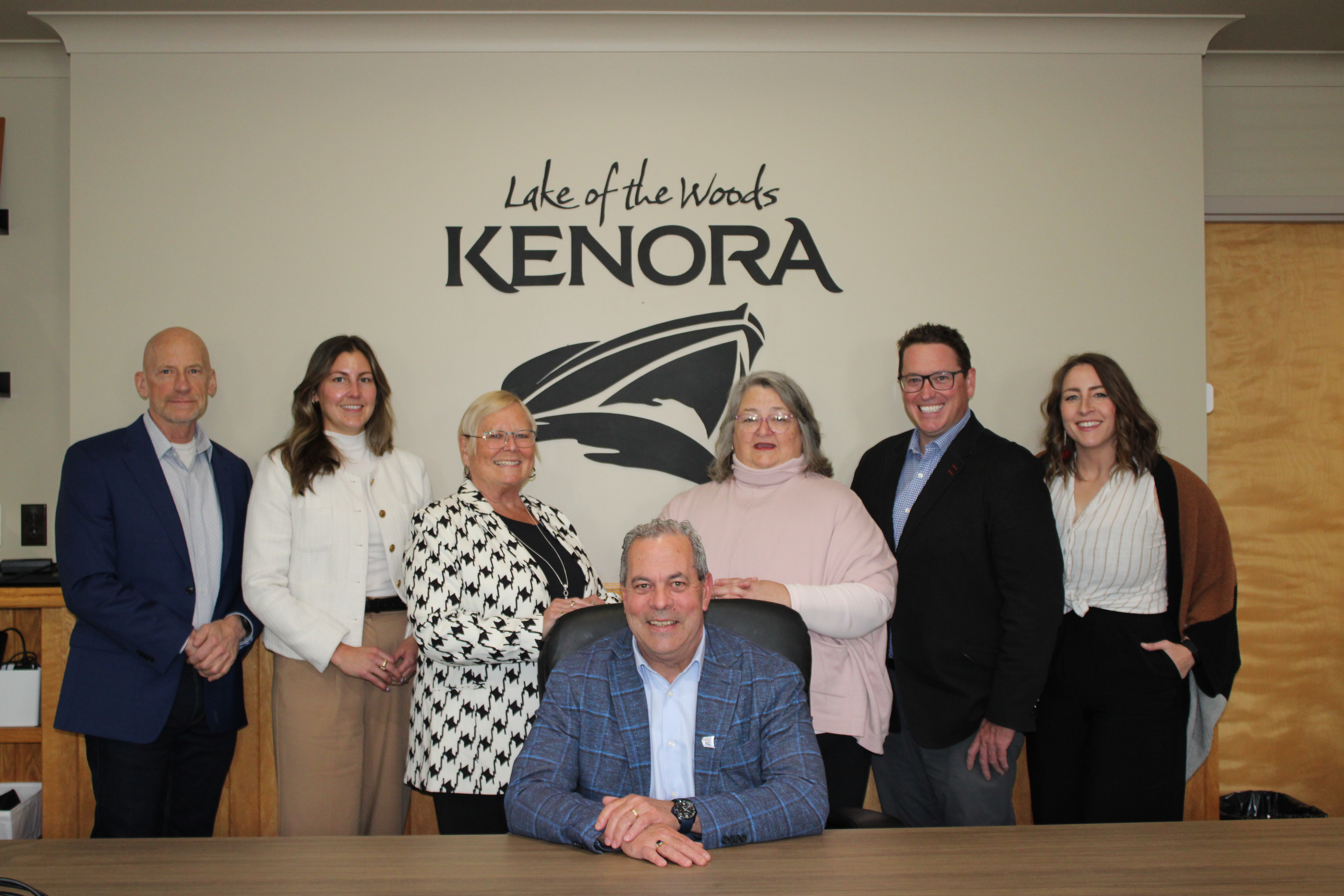 Four women and two men standing behind one man sitting at desk. The flags of Canada and Ontario are on the wall behind the group.