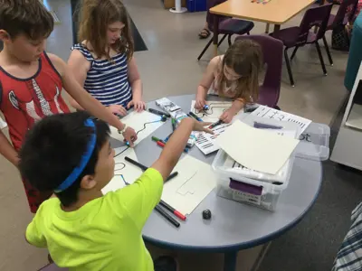 A group of four children sit around a table using Ozobots to explore coding.