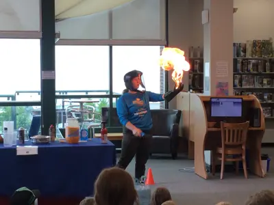 A Science North presenter with a full face shield holding a large fireball in their hand during a science demonstration.