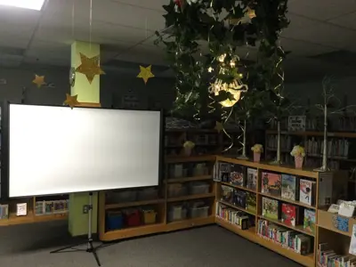 A darkened scene of the Children's Department with a large projector screen, and glittery stars hanging from the ceiling for the Drive-In Movie event.
