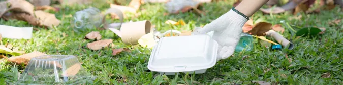 [A hand picking up a food container from the grass.] 