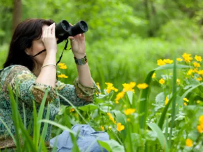 A Woman in a field of grass looking through binoculars.