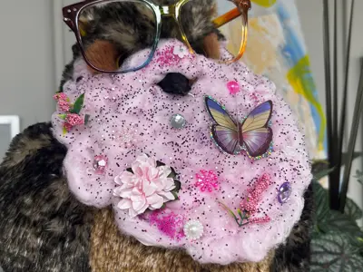 Library's mascot, a stuffed owl named Atticus, is wearing rainbow glasses and a pink glitter beard for Pride month.