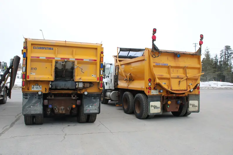 View of the back of 2 plow trucks with the names Clearopathra and Adam Sander decalled on the back